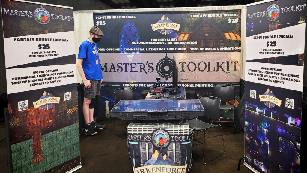 The Arkenforge booth at Gencon 2021. Pullup banners on the sides and a large printed background depicting sales for bundles for 25 dollars.